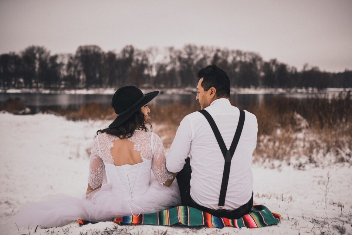 Mexican bride and groom in wedding clothes and suspenders sit on the snow in winter
