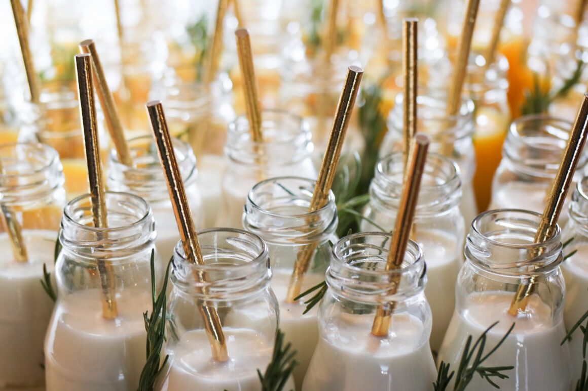 Milk in reusable glass bottles with golden drinking straws at the wedding party.