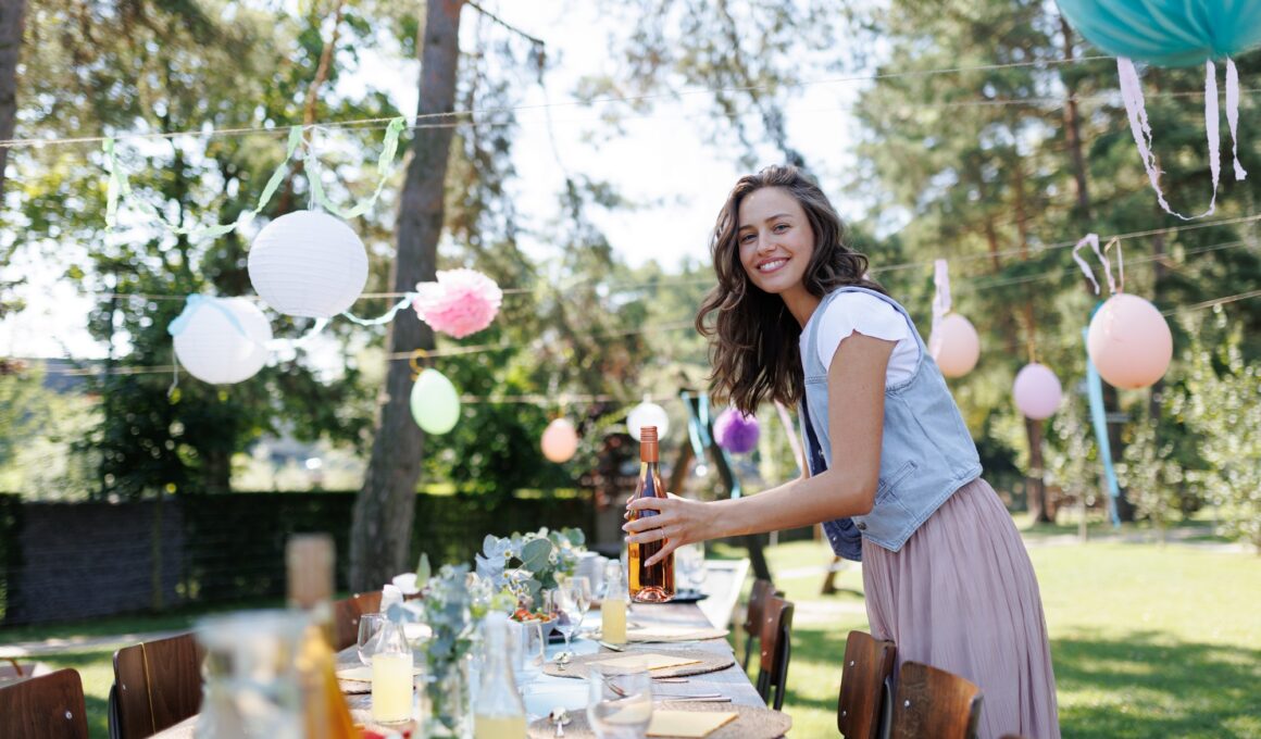 Young beautiful woman preparing refreshments for summer garden party. Hostess is holding bottles of