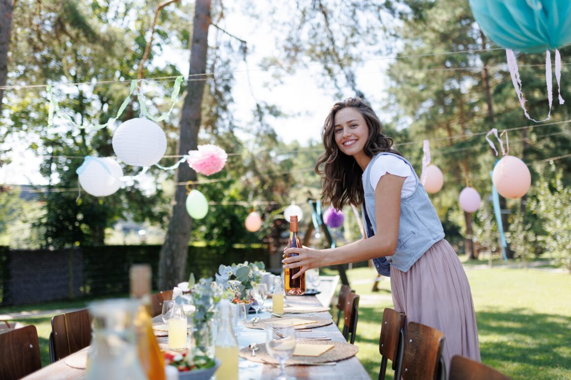 Young beautiful woman preparing refreshments for summer garden party. Hostess is holding bottles of