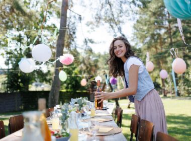 Young beautiful woman preparing refreshments for summer garden party. Hostess is holding bottles of