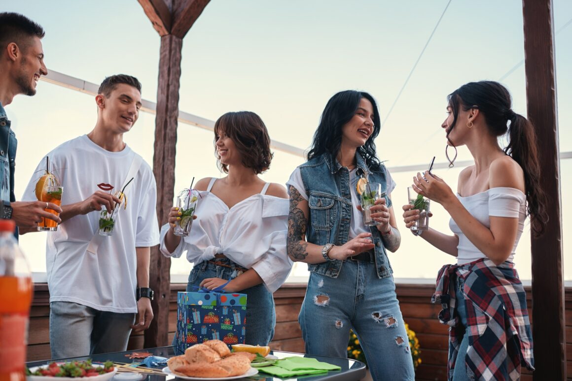 It's my birthday. Cheerful young people chatting and drinking cocktails at a rooftop party