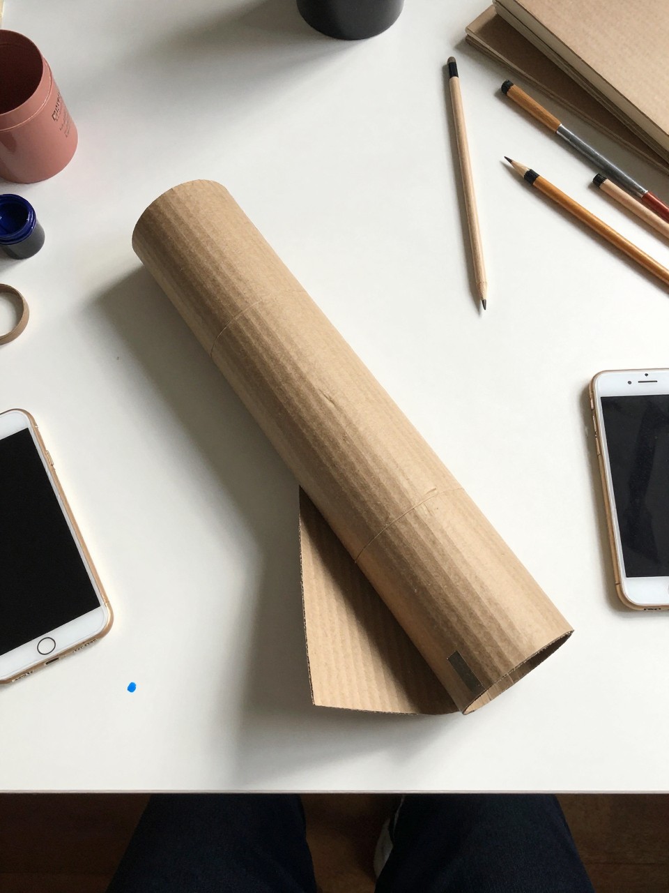 Photo of a cardboard tube pilot craft on a table, overhead flat lay, setting: a white table with scattered art supplies, lighting: natural morning light, containing one lived-in detail: a blue paint smear on the table, iPhone photo quality.