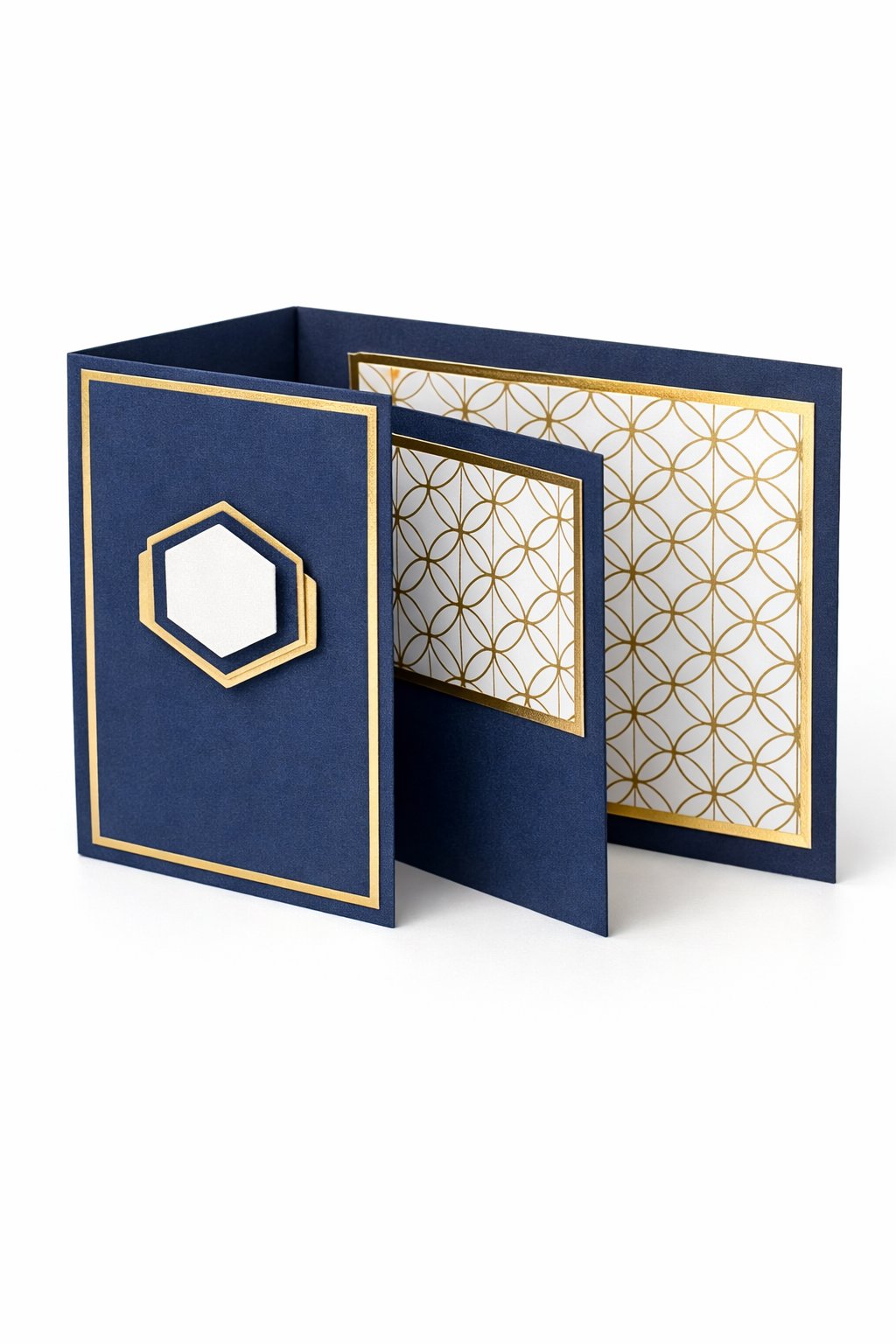 Ultra realistic product photo of a handmade double Z fold card, shown slightly open to display the fold structure, deep navy base with white and gold geometric pattern paper on the panels, thin gold foil border frames on the front and middle panels (no letters), one simple layered hexagon embellishment on the front, crisp folds, matte cardstock texture, photographed on a clean white background with soft studio lighting, no hands, no text, no watermark, sharp focus, high clarity.