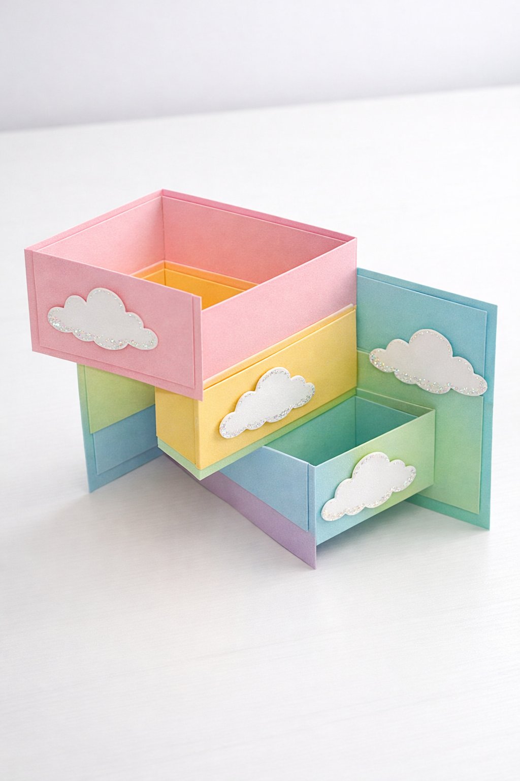 Ultra realistic product photo of a handmade double Z fold card, shown partially open to clearly show the fold structure, pastel rainbow color palette, panels layered with soft rainbow gradient paper and small cloud cutouts, subtle glitter accents on edges only (no words), clean crisp folds, matte cardstock texture, photographed on a bright white tabletop with soft natural light, minimal props, no hands, no text, no watermark, sharp focus, high detail.