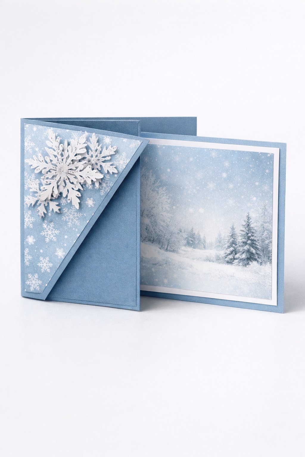 Ultra realistic product photo of a handmade joy fold card, shown slightly open to clearly display the wrap and inner card, icy blue and white winter theme, snowflake patterned paper on the wrap front, layered white snowflake cutouts on the wrap flap corner with subtle silver shimmer accents, crisp folds, matte cardstock texture, photographed on a clean bright white surface with cool soft lighting, minimal props, no hands, no text, no watermark, sharp focus, high detail.