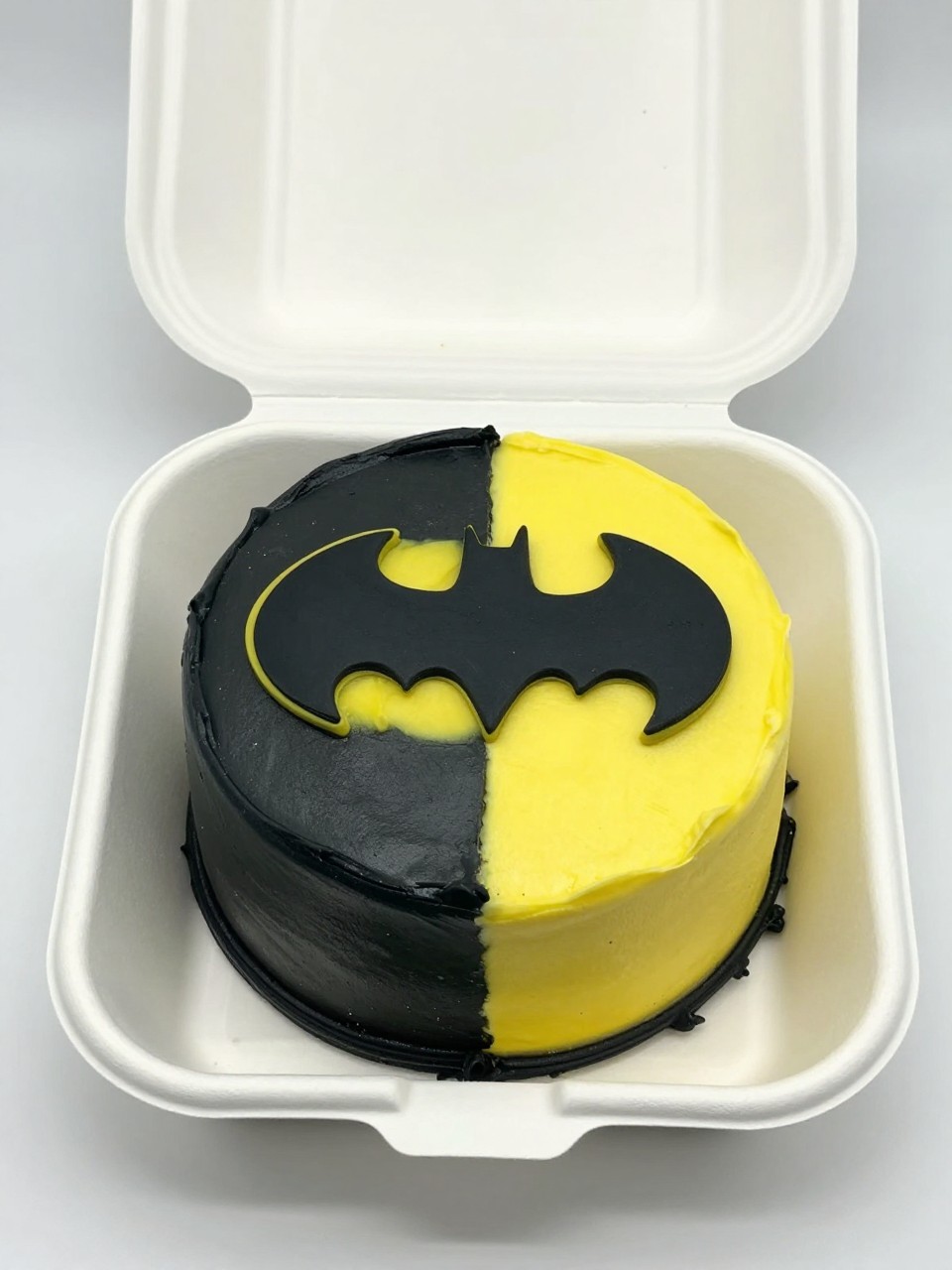 Image Prompt:
A stylish Batman inspired bento cake in an open white cake box, small round cake split into two halves with smooth black frosting on one side and bright yellow frosting on the other, centered Batman symbol bridging both halves, neat border, modern superhero styling, realistic bakery photo, no people, no hands, no faces, (no watermarks on images)