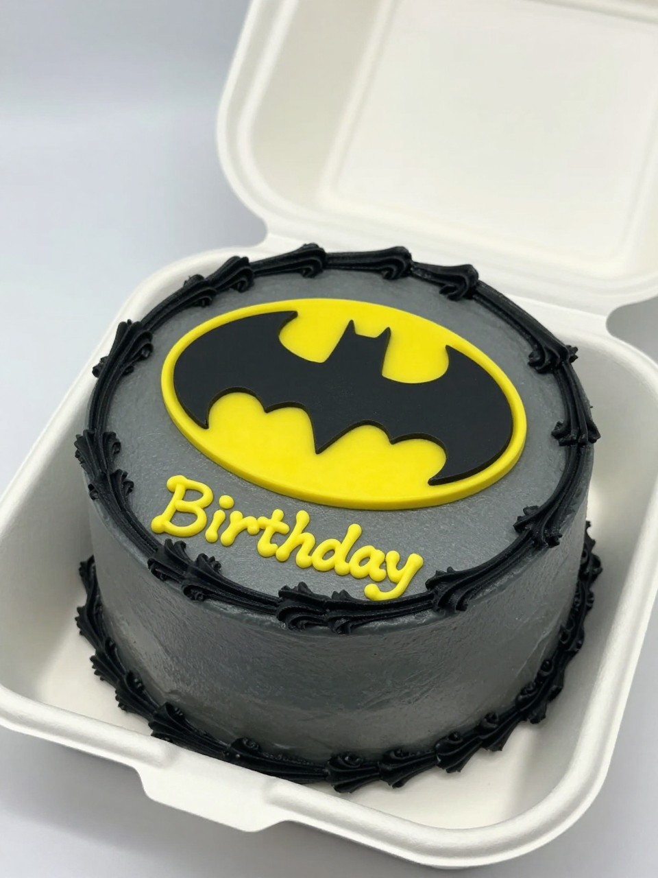 Image Prompt:
A personalized Batman themed bento cake inside an open white bento cake box, smooth charcoal gray frosting, bright yellow Batman symbol at the top, a first name written neatly in yellow icing below, black piped border, modern birthday styling, realistic close-up bakery photography, no people, no hands, no faces, (no watermarks on images)