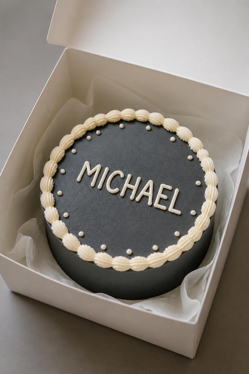 Image Prompt:
A personalized bento cake for men inside an open white cake box, smooth charcoal gray frosting, neat cream piped border, one masculine first name written clearly in white icing, tiny dot accents around the edge, clean minimal dessert styling, soft studio light, realistic bakery photography, no people, no hands, no faces, no watermarks on images