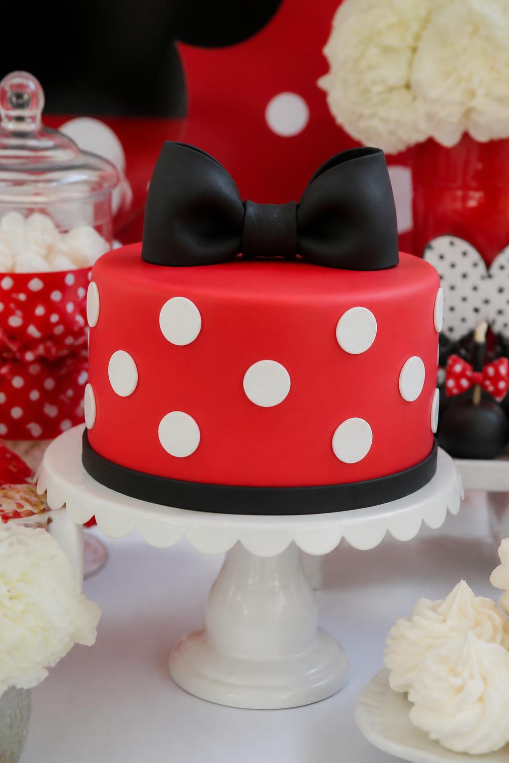 Detailed Image Prompt:
A cute red and white polka dot cake inspired by classic cartoon party styling, smooth red fondant base with white dots, black fondant bow topper, simple black trim, styled on a bright birthday dessert table, playful editorial cake photography, no people, realistic DSLR photo, no copyrighted character face or logos, no watermarks on images.