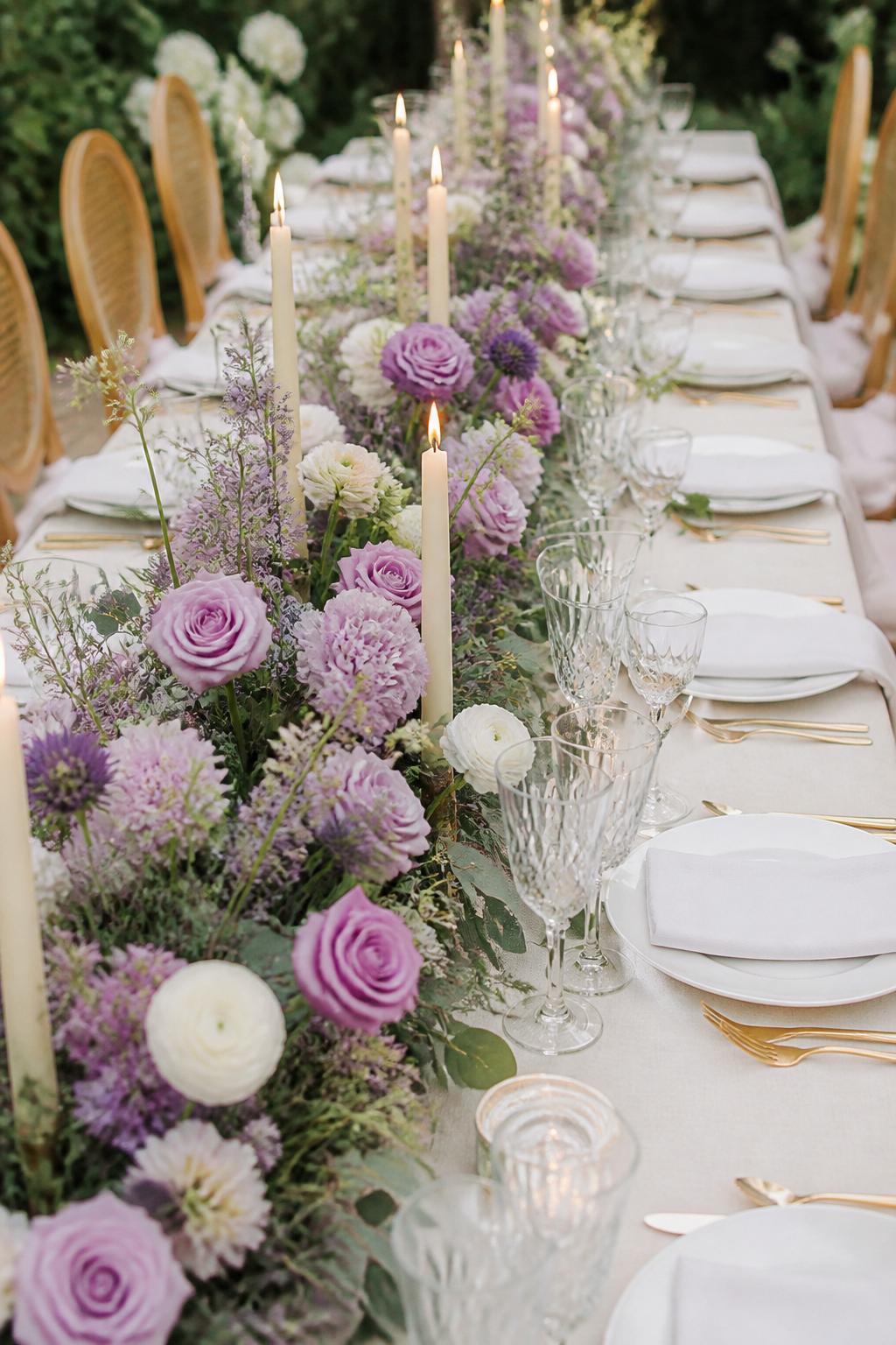 Image Prompt:
A beautiful wedding reception table photo showing a long table with a lilac floral runner running down the center, using lilac roses, lavender blooms, white ranunculus, soft greenery, and ivory taper candles. Add white plates, gold flatware, crystal glasses, and ivory linen. Romantic garden wedding setting, no visible faces, no text, no watermark, realistic DSLR editorial photography, (no watermarks on images)