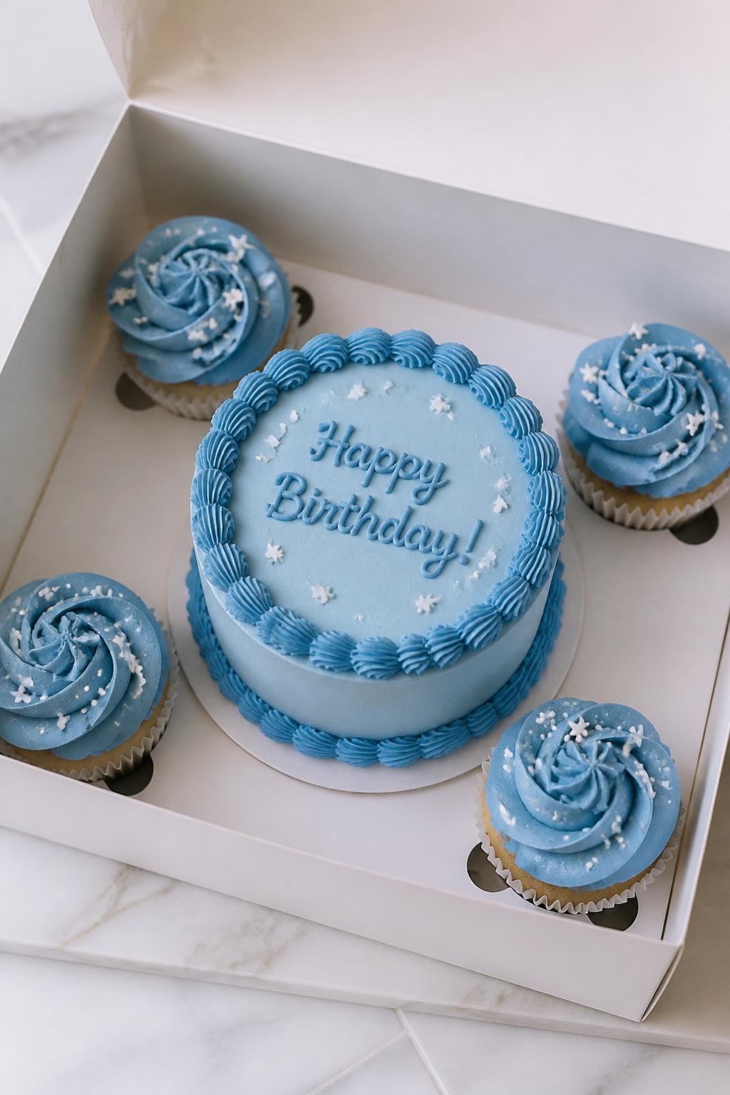Image Prompt:
A beautiful blue birthday bento cake with cupcakes set in a white gift box, one small bento cake in the center with smooth baby blue frosting, darker blue piped border, and handwritten birthday text, surrounded by four matching cupcakes with blue buttercream swirls and tiny white star sprinkles, clean modern styling, bright natural light, realistic editorial dessert photography, no people, no hands, no faces, no watermarks on images