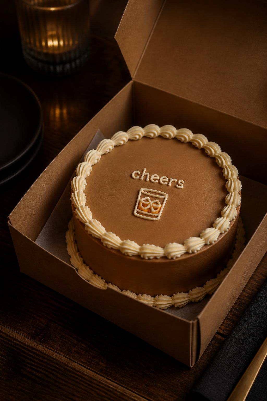 Image Prompt:
A classy cheers themed bento cake for men inside an open kraft cake box, smooth warm brown buttercream frosting, small buttercream whiskey glass icon on top, short icing text reading “cheers,” neat cream piped border, moody bar-inspired styling with wooden table surface, realistic editorial dessert photography, no alcohol bottles, no people, no hands, no faces, no watermarks on images