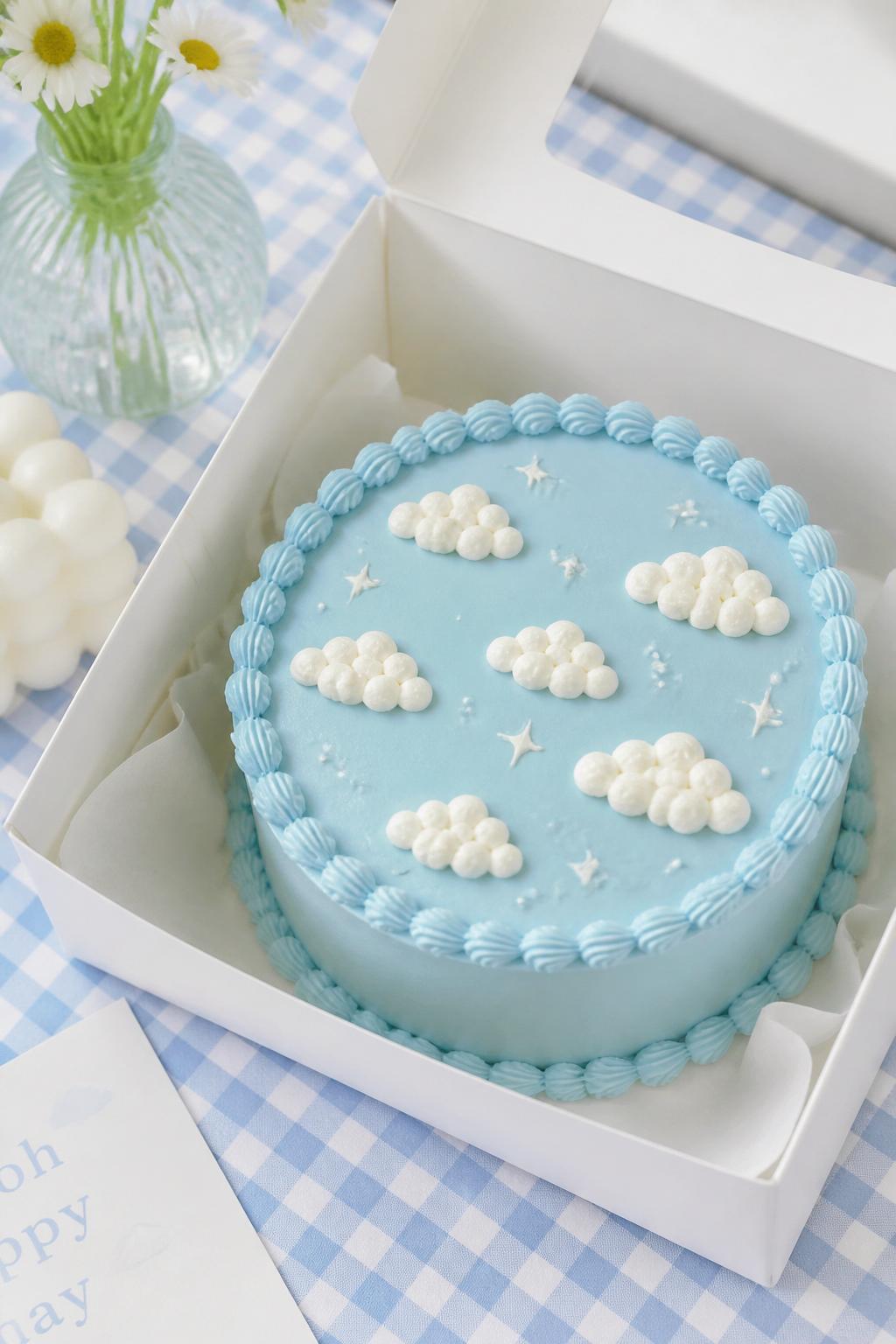 Image Prompt:
A cute cloud themed blue bento cake inside an open white cake box, smooth sky blue frosting, tiny fluffy white buttercream clouds on top, soft piped border, dreamy playful styling, bright natural light, pastel setup, realistic editorial bakery photography, no people, no hands, no faces, (no watermarks on images)