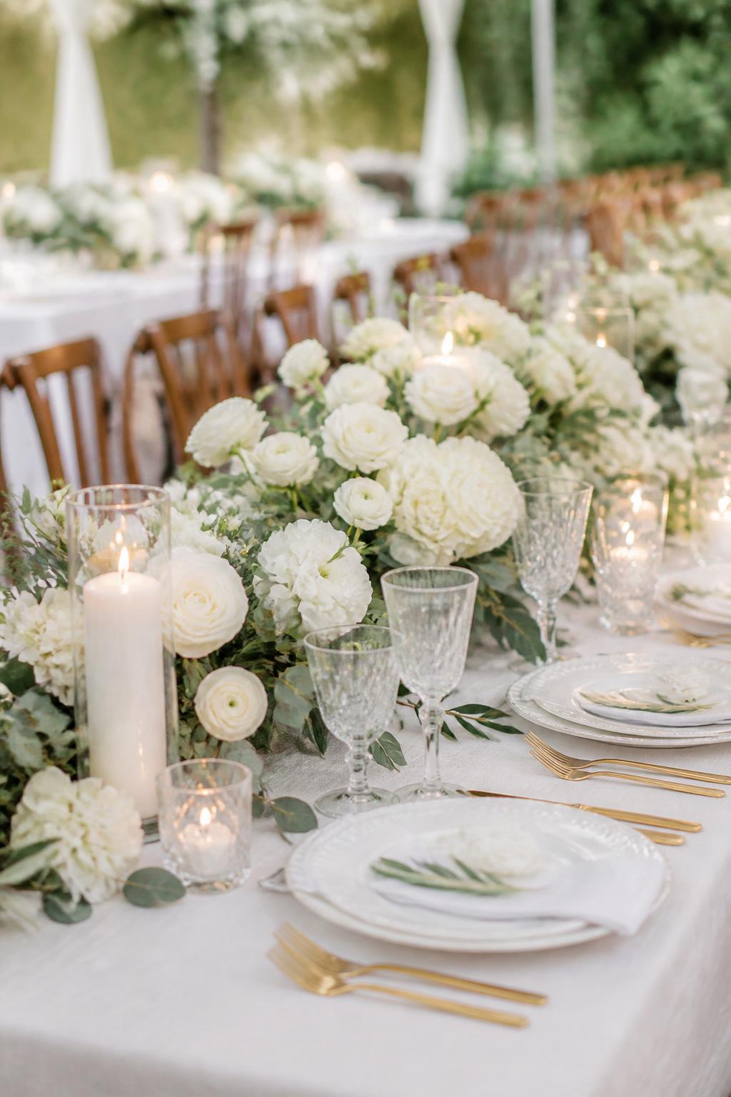 Image Prompt:
A fresh editorial wedding table photo showing white roses, white hydrangeas, white ranunculus, eucalyptus, olive branches, ivory candles, white plates, gold flatware, and clear crystal glasses on a long reception table. Outdoor garden or tented wedding setting, no visible faces, no text, no watermark, professional DSLR photography, (no watermarks on images)