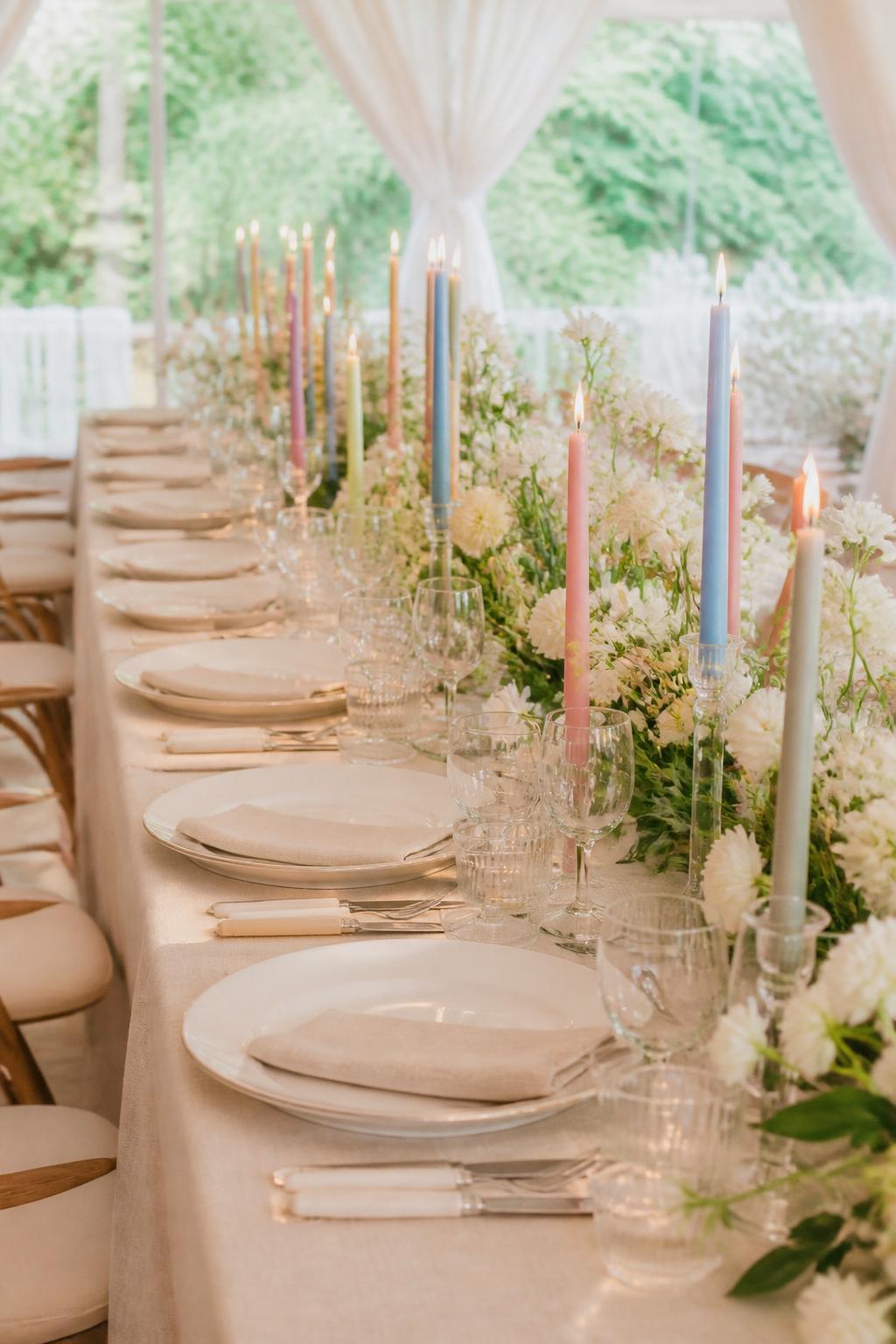 Image Prompt:
A joyful whimsical wedding table featuring taper candles in soft pastel colors, including blush, lavender, pale yellow, sage, and soft blue, paired with simple white flowers, clear glassware, white plates, and neutral linen. Bright garden or tented reception setting, no visible faces, no text, no watermark, realistic wedding magazine photography, (no watermarks on images)