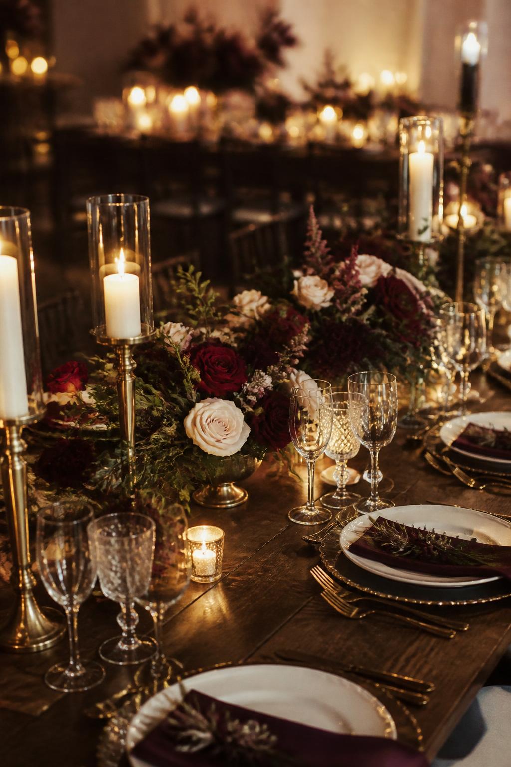 Image Prompt:
A romantic wedding reception table styled with low floral centerpieces in burgundy, plum, deep red, and soft ivory tones, paired with dark greenery, gold candle holders, white plates, gold flatware, crystal glasses, and warm candlelight. Elegant evening reception setting, no visible faces, no text, no watermark, realistic DSLR wedding photography, (no watermarks on images)