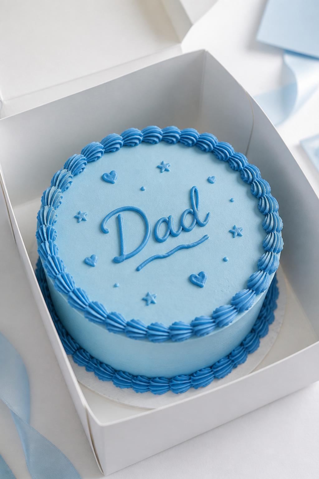 Image Prompt:
A beautiful monochrome blue Father’s Day bento cake inside an open white cake box, smooth baby blue frosting, darker blue piped border, blue handwritten icing text reading “Dad,” tiny blue heart and star details, modern tone-on-tone styling, bright clean backdrop, realistic editorial dessert photography, no people, no hands, no faces, no watermarks on images