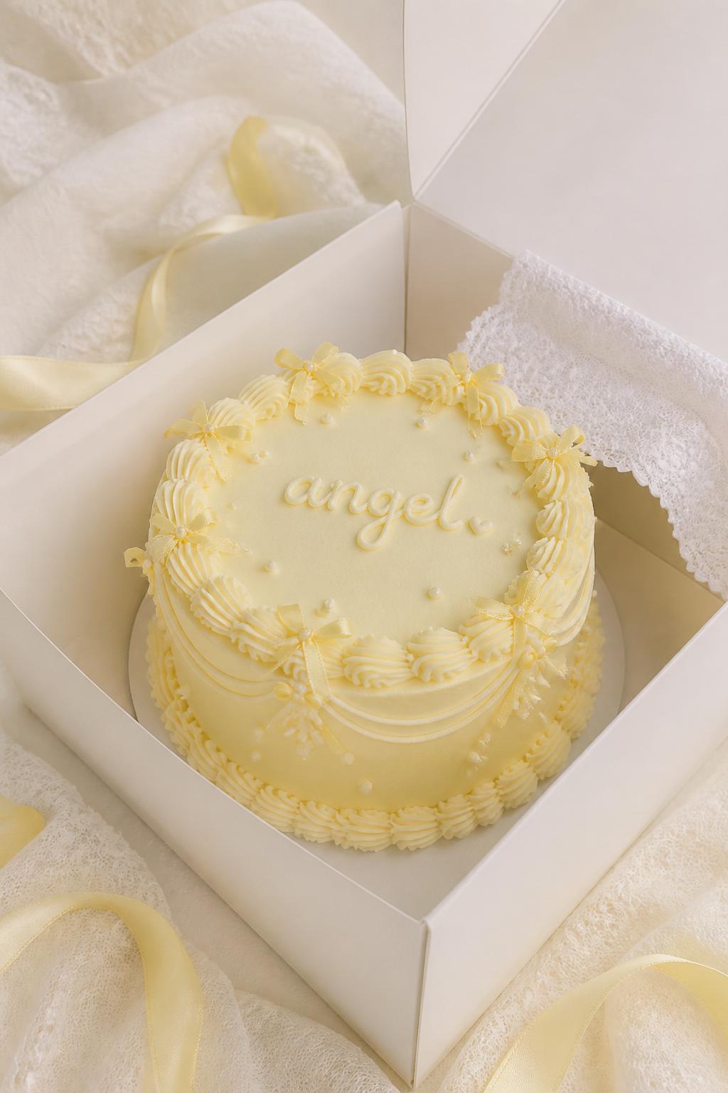 Image Prompt:
A coquette inspired yellow ribbon bento cake in an open white cake box, pale butter yellow frosting, tiny ribbon bow details, pearl accents, delicate scalloped border, handwritten icing text reading “angel,” soft lace inspired styling, editorial bakery photography, no people, no hands, no faces, no watermarks on images