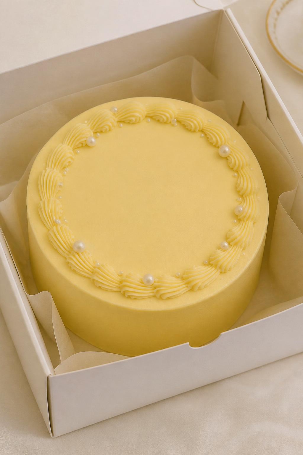 Image Prompt:
A beautiful yellow pearl bento cake inside a white cake box, smooth dusty yellow frosting, tiny edible pearl accents placed neatly around the top edge, elegant piped border, soft luxury bakery styling, clean backdrop, realistic editorial dessert photography, no people, no hands, no faces, no watermarks on images