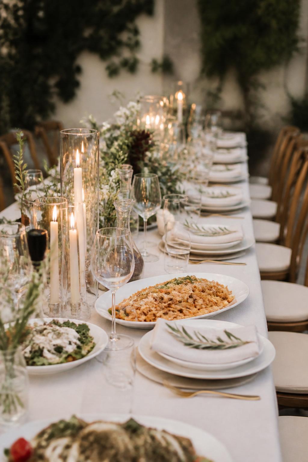 Image Prompt:
A warm editorial wedding dinner table styled for family style dining with elegant shared pasta platters, wine glasses, ceramic plates, linen napkins, small floral arrangements, candles, and greenery. Italian-inspired garden or courtyard reception setting, no visible faces, no full people, no readable text, no watermark, realistic DSLR wedding photography, (no watermarks on images)