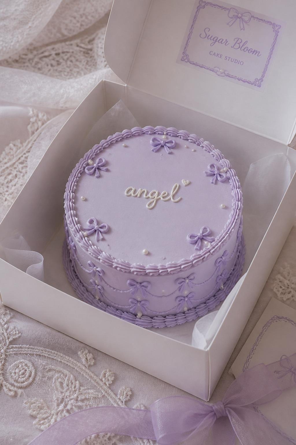 Image Prompt:
A coquette inspired purple ribbon bento cake in an open white cake box, baby lavender frosting, tiny ribbon bow details, pearl accents, delicate scalloped border, handwritten icing text reading “angel,” soft lace inspired styling, editorial bakery photography, no people, no hands, no faces, (no watermarks on images)