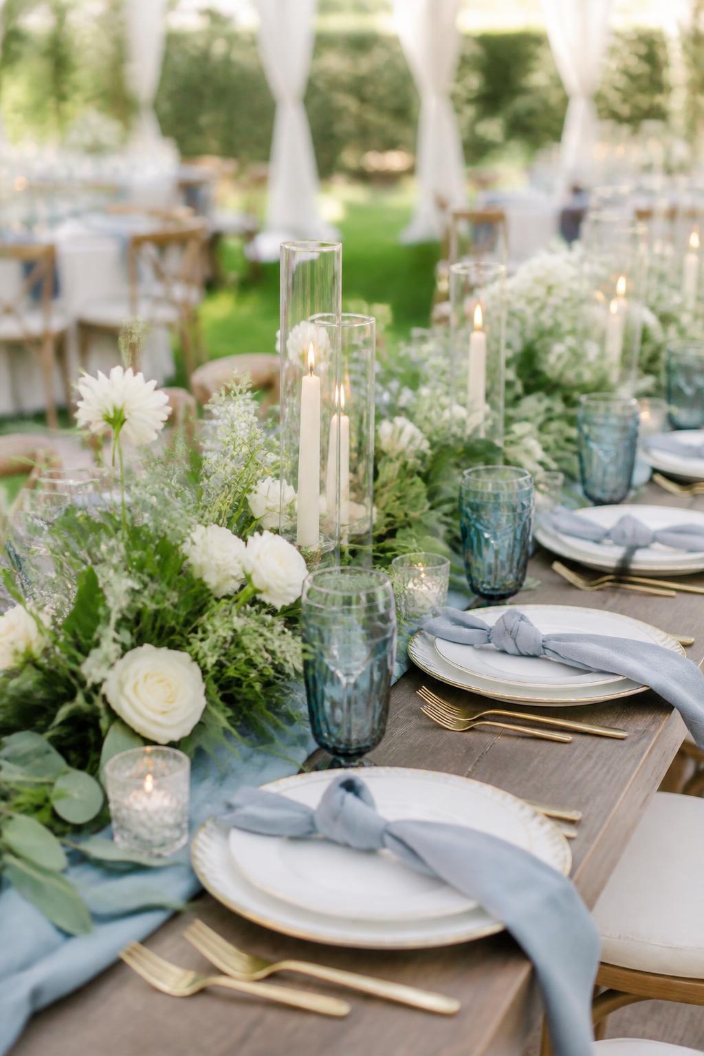 Image Prompt:
A beautiful garden wedding table showing soft blue napkins, lush greenery, white flowers, blue glassware, ivory candles, white plates, and gold flatware on a long reception table. Outdoor garden or tented wedding setting with soft natural light, no visible faces, no text, no watermark, realistic editorial wedding photography, (no watermarks on images)