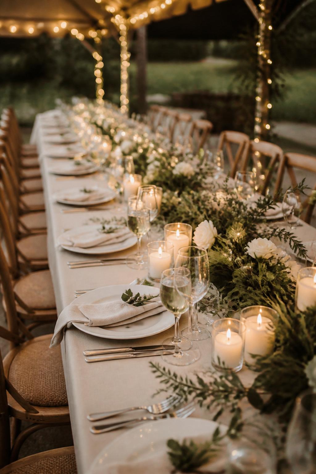 Image Prompt:
A magical wedding table photo showing a long reception table with a soft greenery garland woven with tiny warm fairy lights, white flowers, ivory candles, white plates, clear glassware, and neutral linen napkins. Evening garden or tented reception setting, no visible faces, no text, no watermark, realistic editorial wedding photography, (no watermarks on images)