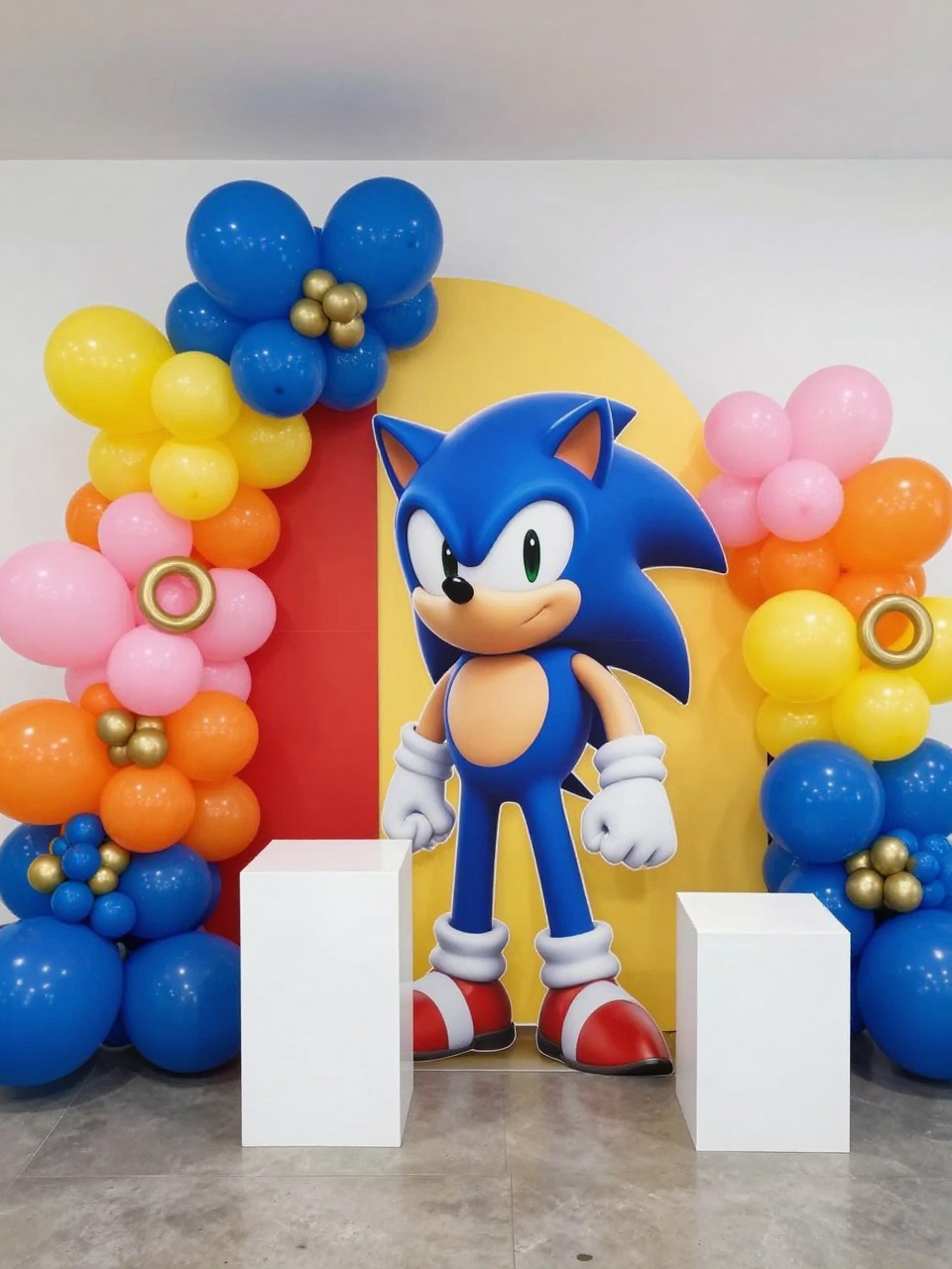 Image Prompt:
A single realistic editorial photo of a Sonic-inspired birthday party backdrop using character-inspired color zones, with royal blue, red, yellow, pink, and orange curved panels, matching balloon clusters, gold ring props, white plinths, playful indoor party space, no people, no faces, bright clean lighting, realistic event photography, no readable text, no watermark.