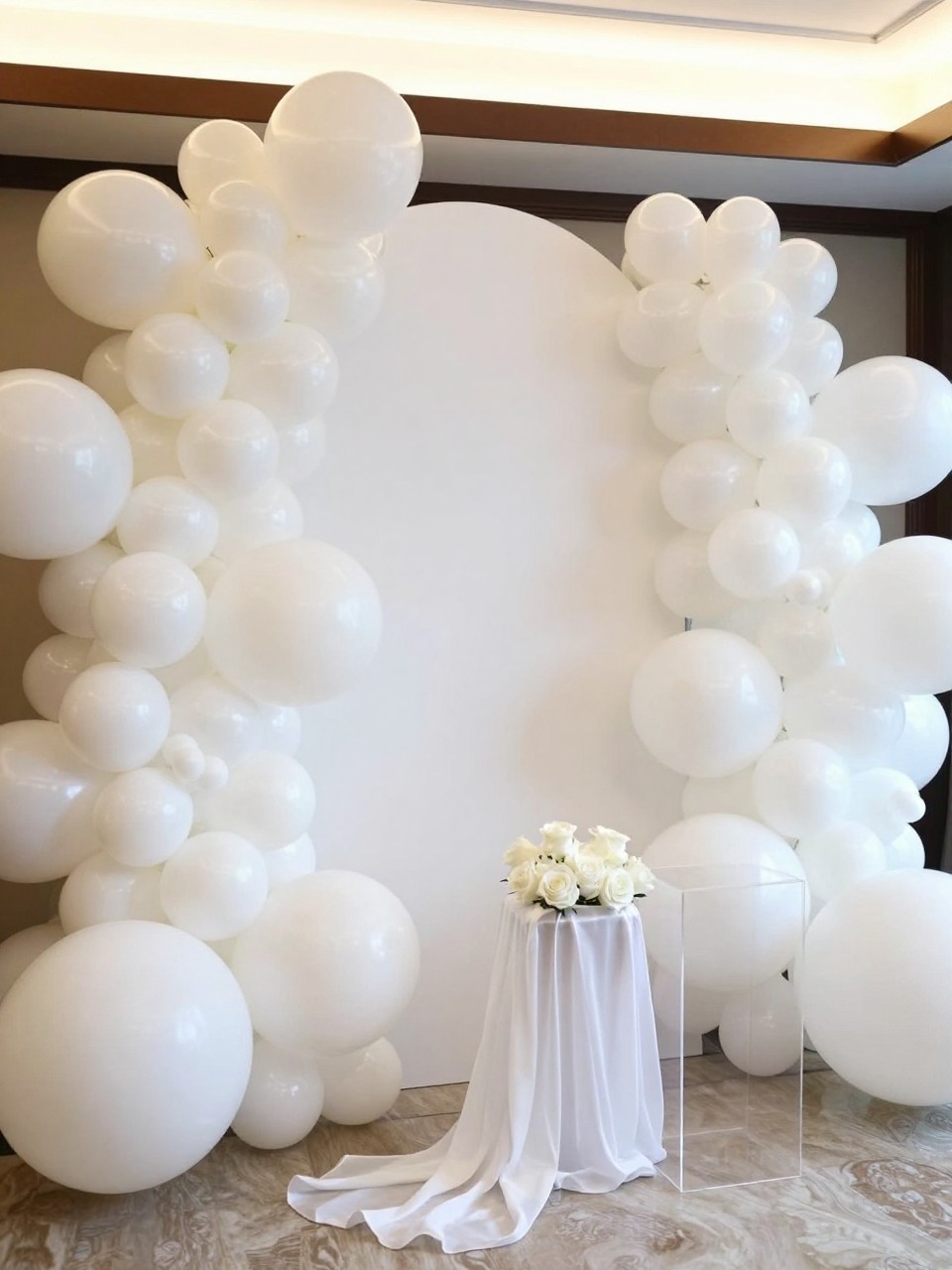 Image Prompt:
A single realistic editorial-style photo of an elegant all-white balloon backdrop with pearl white balloons in different sizes arranged around a white curved panel, white roses at the base, clear acrylic plinths, soft sheer fabric draping, warm natural indoor light, no people, no faces, clean luxury event photography, no text, no watermark.
