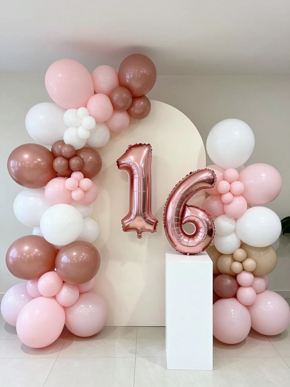 Image Prompt:
A single realistic photo of a Sweet 16 party backdrop with a full balloon installation in rose gold, blush pink, white, and soft beige, a cream arch panel in the center, large metallic number 16 balloons, white plinths, polished indoor party room, no people, no faces, bright soft lighting, realistic birthday photography, no text, no watermark.