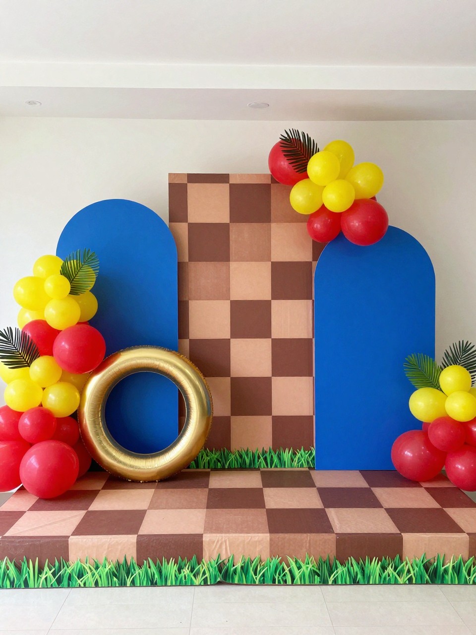 Image Prompt:
A single realistic photo of a Sonic party backdrop with a brown and tan checkered platform-style wall, bright blue arched panel, green grass trim at the base, gold ring props, red and yellow balloon clusters, small palm leaves, indoor birthday party setup, no people, no faces, realistic playful event photography, no text, no watermark.