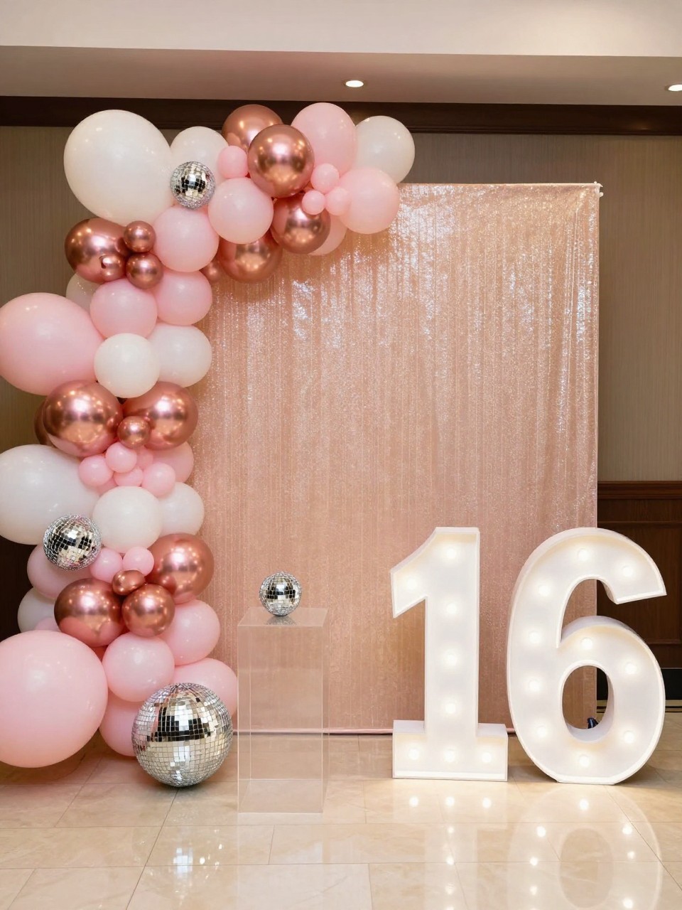 Image Prompt:
A single realistic photo of a glamorous Sweet 16 backdrop with a champagne shimmer wall, blush pink, white, and rose gold balloon garland, small disco balls at the base, clear acrylic plinths, a large number 16 prop, polished indoor party setting, no people, no faces, warm indoor lighting, realistic glossy event photography, no text, no watermark.