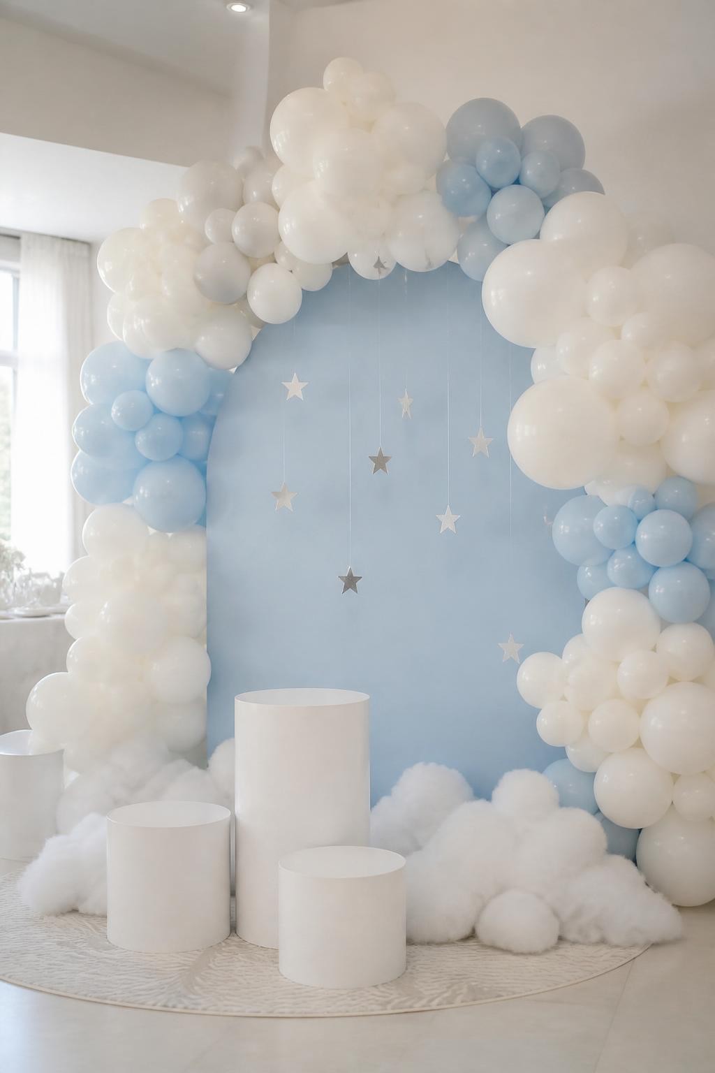 Image Prompt:
A single realistic photo of a dreamy balloon cloud arch backdrop with white and pale blue balloons arranged in soft cloud-like clusters around a light blue arch panel, fluffy faux cloud props at the base, small silver star cutouts hanging from clear thread, white plinths in front, airy indoor party room, no people, no faces, bright soft lighting, realistic party photography, no text, no watermark.
