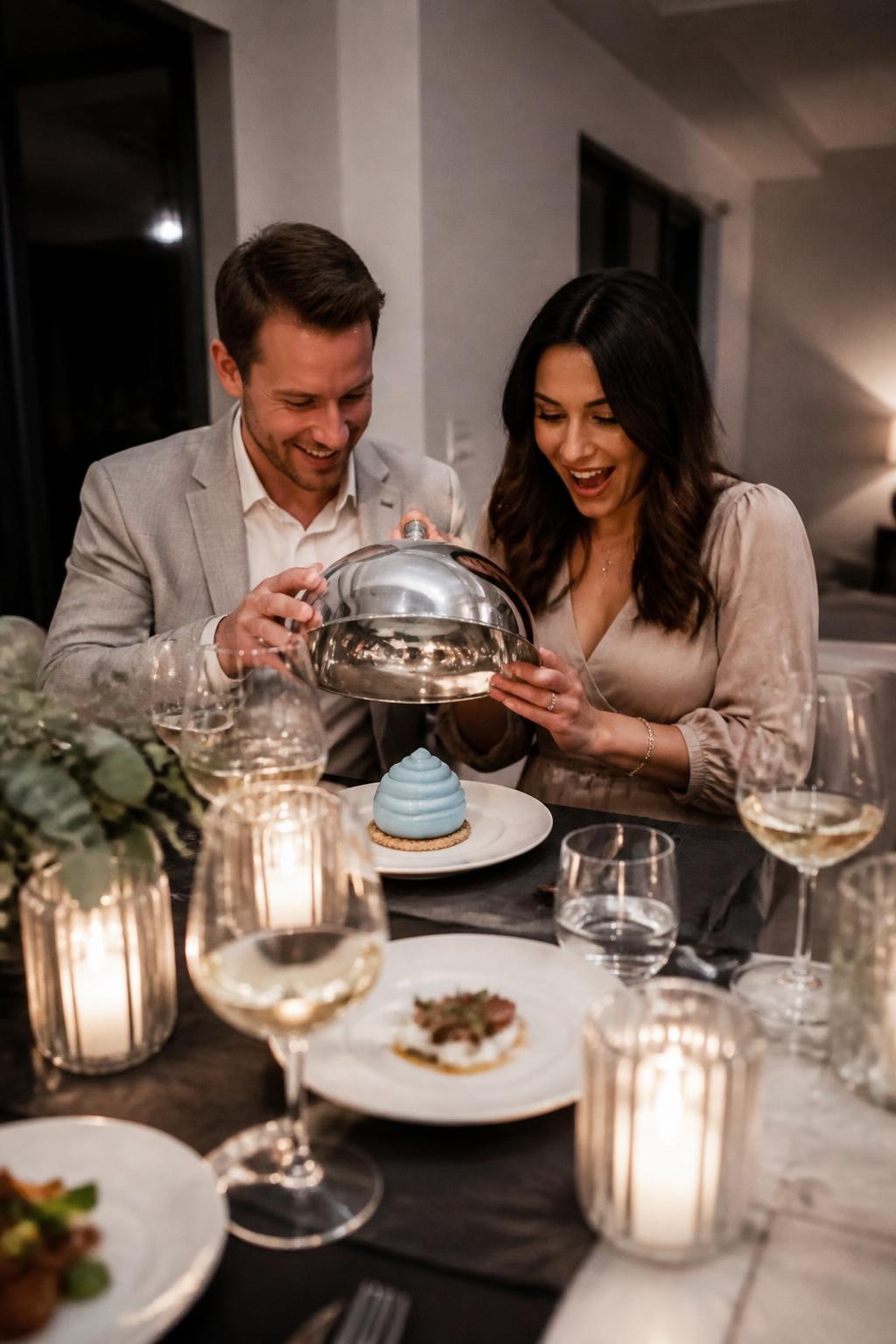 A realistic editorial photo of a cozy upscale at-home dinner gender reveal, beautifully plated tasting menu on a modern dining table, soft candles, elegant glassware, neutral decor, parents lifting a cloche to reveal a final dessert in one reveal color, intimate and stylish atmosphere, realistic DSLR photography