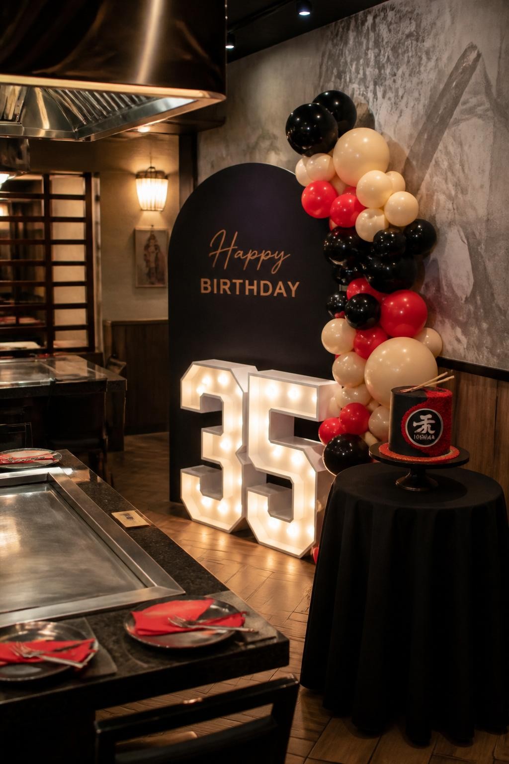 Image Prompt:
A realistic DSLR photo of a hibachi birthday party setup with a modern number display beside the grill area, coordinated balloons in black, cream, and red, a compact cake table, and warm indoor party lighting, no people, stylish celebratory event decor.