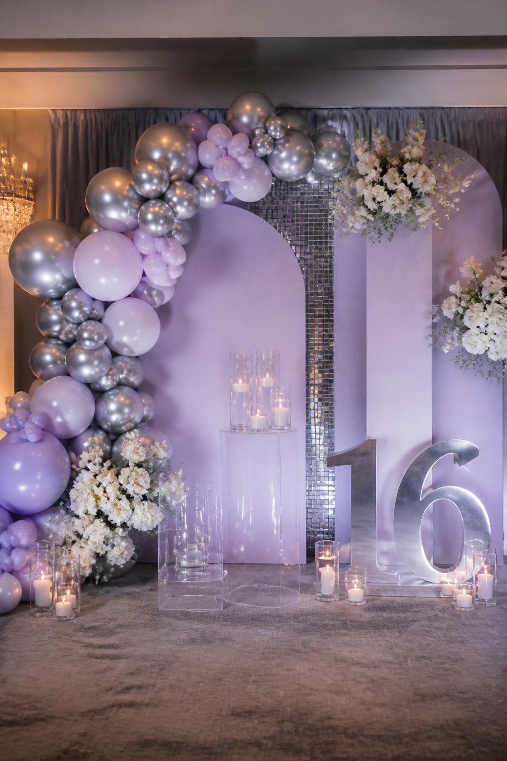 Image Prompt:
A single realistic photo of a pretty Sweet 16 backdrop with lavender curved panels, silver balloon garland, white flowers, clear plinths, candle clusters, a silver number 16 prop, elegant indoor party setting, no people, no faces, soft flattering lighting, realistic upscale birthday photography, no text, no watermark.