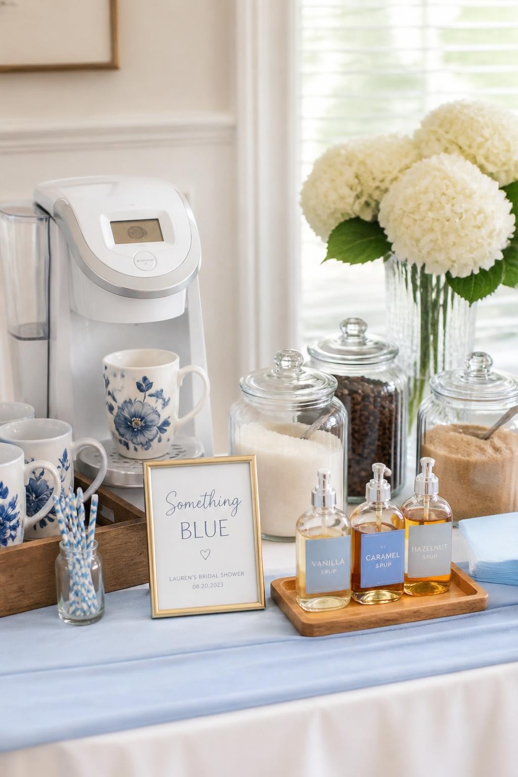 A realistic DSLR photo of a bridal shower coffee bar with a soft blue and white theme, pale blue table runner, white coffee machine, blue floral mugs, glass jars of sugar and coffee beans, small blue syrup labels, white hydrangeas in a vase, tiny sign reading something blue, bright natural light, airy elegant home event styling, no people.