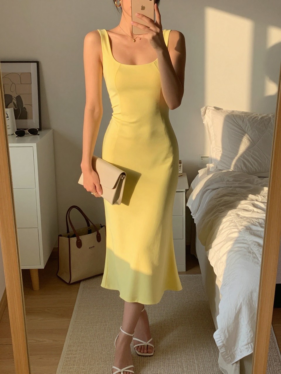 Image prompt
mirror selfie of a woman wearing a sunshine yellow midi dress with white strappy heels, a cream clutch, and gold hoop earrings, holding a phone in front of a mirror, cropped at NECK so face doesn't show, with a natural casual selfie pose, in a feminine-themed bedroom, evening golden hour, including small lived-in details like a tote bag on the floor, sunglasses on a dresser, or soft bedding in the background, latest iPhone photo quality.