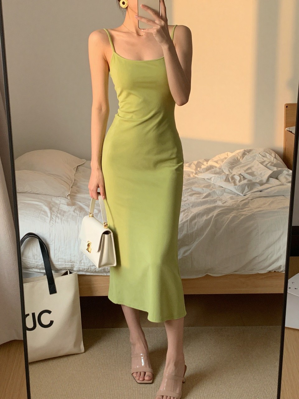 Image prompt
mirror selfie of a woman wearing a lime green midi dress with nude heeled mules, gold statement earrings, and a white mini bag, holding a phone in front of a mirror, cropped at NECK so face doesn't show, with a natural casual selfie pose, in a feminine-themed bedroom, evening golden hour, including small lived-in details like soft bedding and a tote bag on the floor, latest iPhone photo quality.
