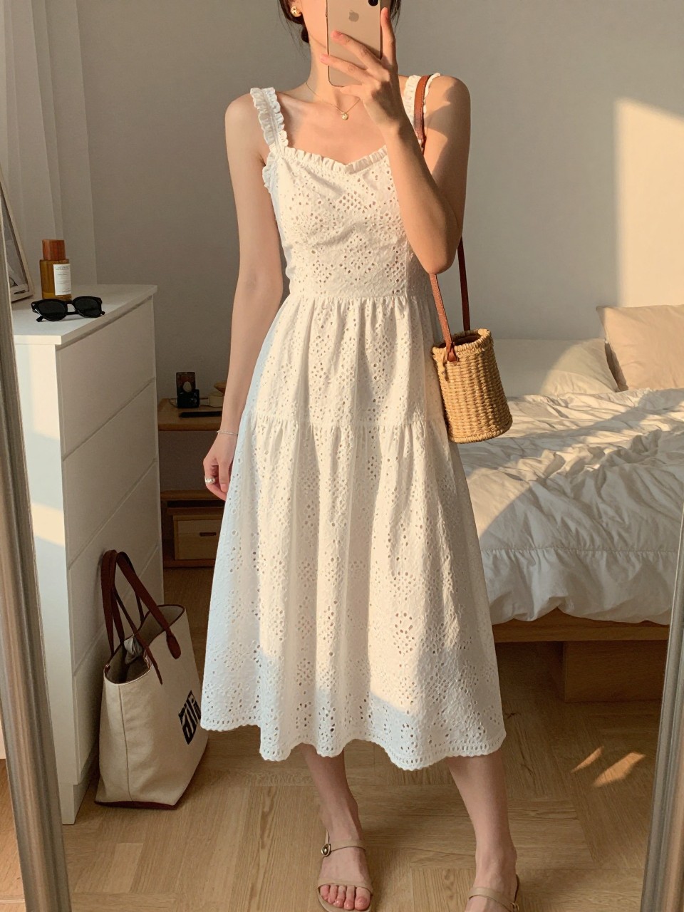 Image prompt
mirror selfie of a woman wearing a white eyelet midi dress with a lined skirt, nude flat sandals, small gold stud earrings, and a small woven mini bag, holding a phone in front of a mirror, cropped at NECK so face doesn't show, with a natural casual selfie pose, in a feminine-themed bedroom, evening golden hour, including small lived-in details like a tote bag on the floor, sunglasses on a dresser, or soft bedding in the background, latest iPhone photo quality.