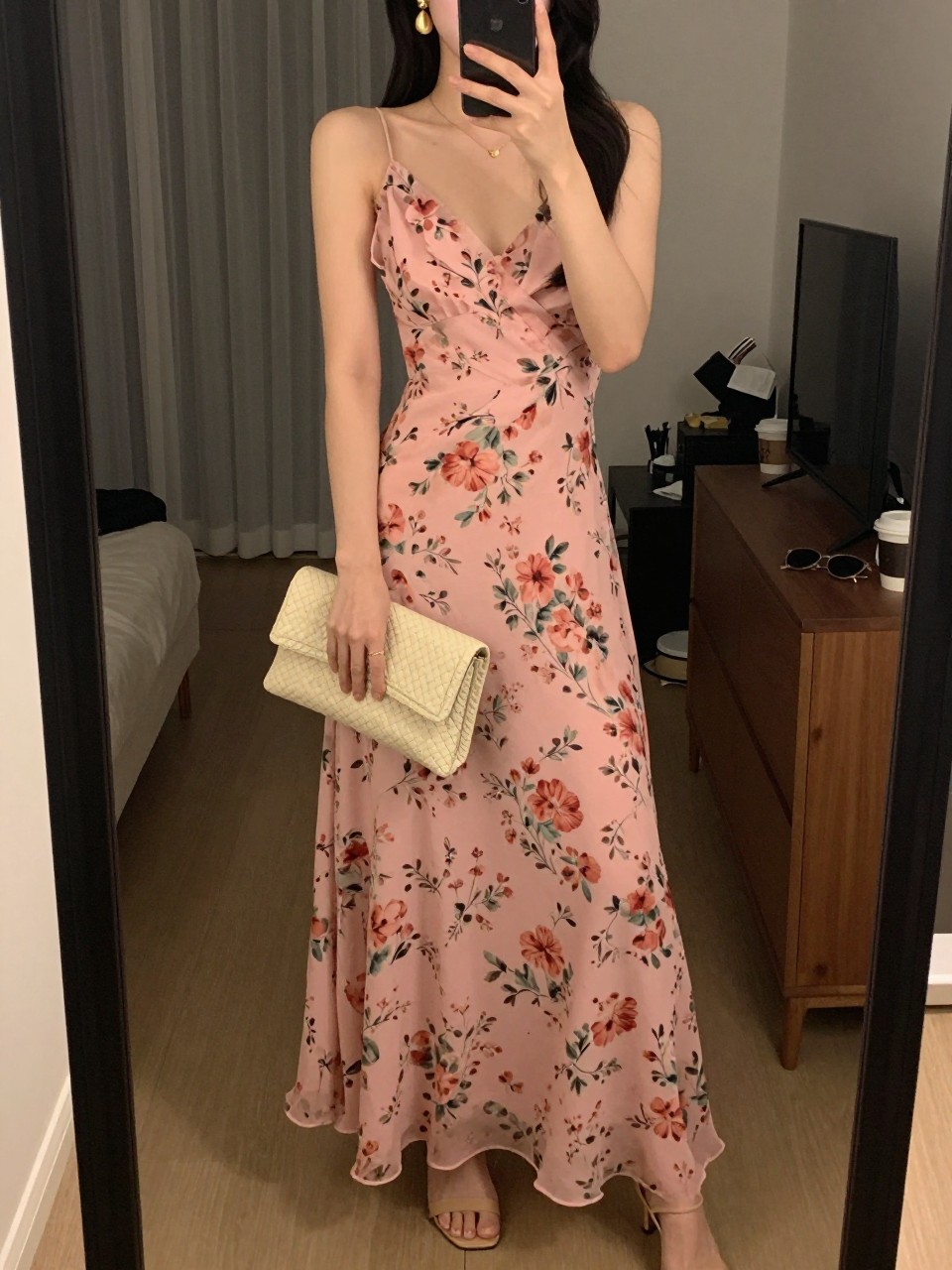 Image prompt
mirror selfie of a woman wearing a pink floral chiffon maxi dress with nude heeled sandals, a cream woven clutch, and gold drop earrings, holding a phone in front of a mirror, cropped at NECK so face doesn't show, with a natural casual selfie pose, in a city apartment, warm moody lighting, including small lived-in details like sunglasses on a dresser and a coffee mug nearby, latest iPhone photo quality.