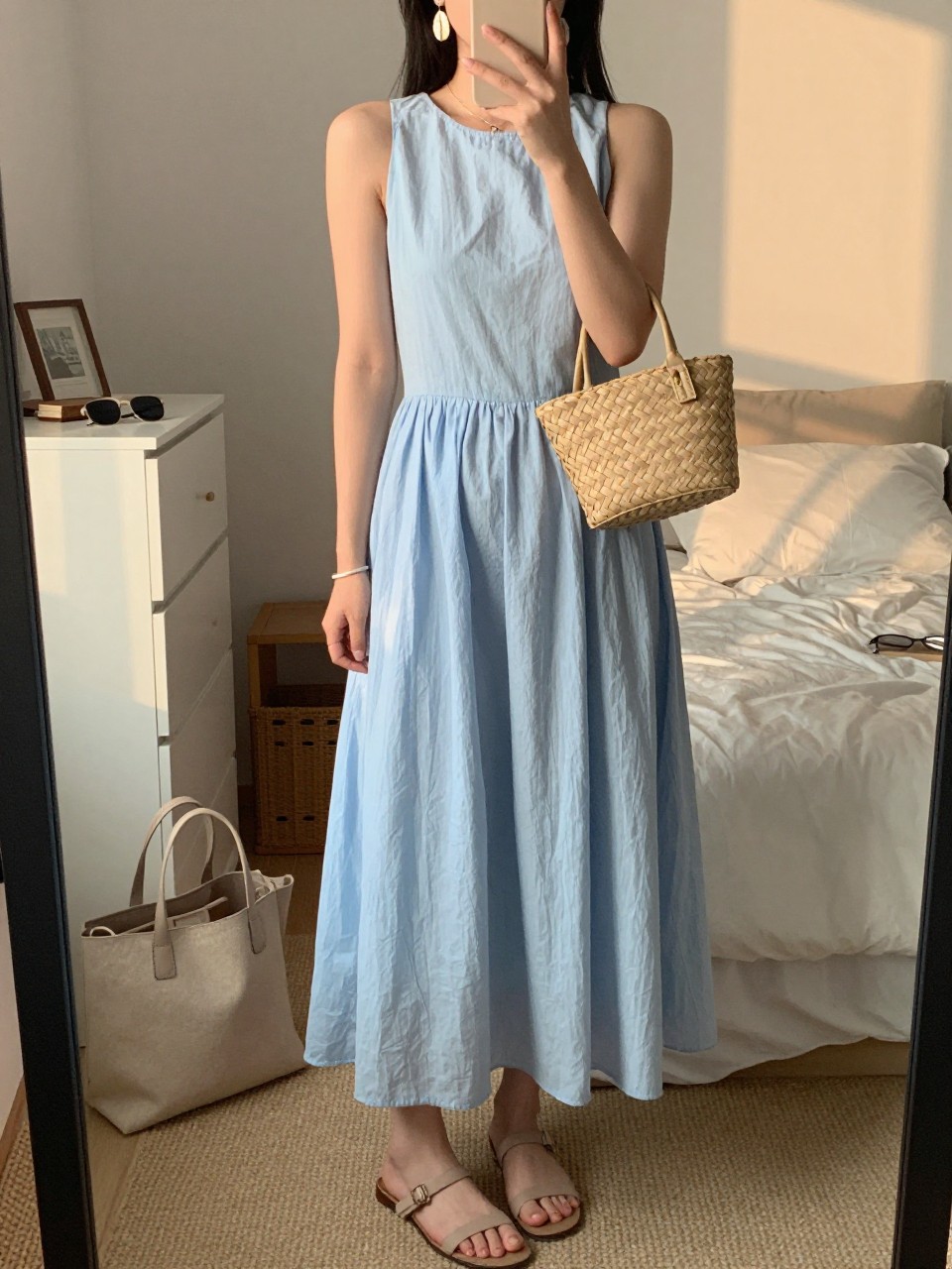 Image prompt
mirror selfie of a woman wearing a light blue cotton maxi dress with a flowy skirt, shell drop earrings, nude flat sandals, and a structured woven mini bag, holding a phone in front of a mirror, cropped at NECK so face doesn't show, with a natural casual selfie pose, in a feminine-themed bedroom, evening golden hour, including small lived-in details like a tote bag on the floor, sunglasses on a dresser, or soft bedding in the background, latest iPhone photo quality.