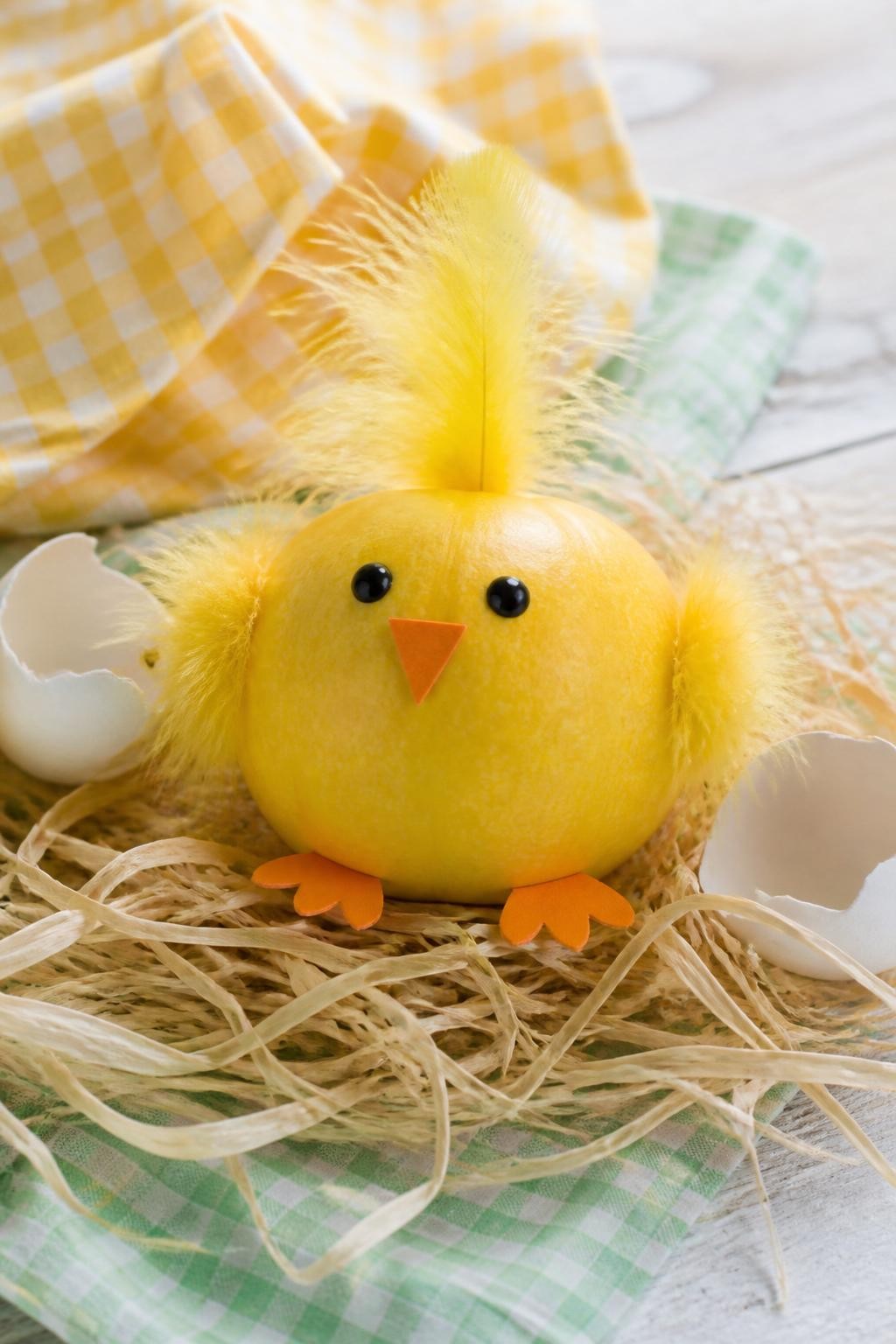 Image Prompt: A realistic DSLR photo of a small yellow pumpkin decorated as a fluffy baby chick, with soft yellow feather pieces, tiny orange paper feet, small orange beak, black dot eyes, sitting in a nest of raffia with cracked eggshell paper pieces, pastel gingham cloth, and bright cheerful natural light, adorable kids fall craft photography.