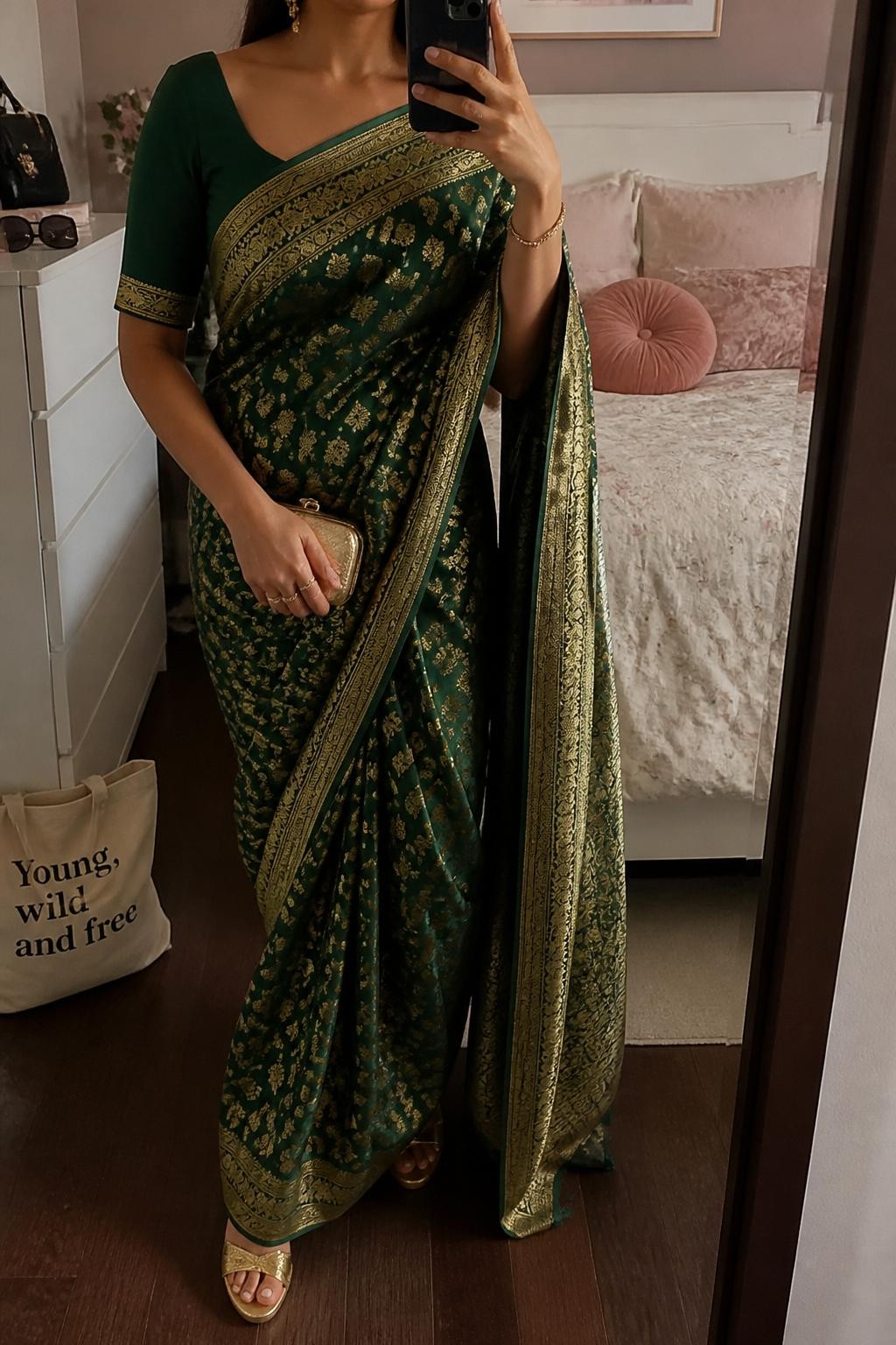 Image prompt
mirror selfie of a woman wearing a deep green Banarasi saree with gold zari and a matching blouse, gold jhumka earrings, gold wedges, and a small gold clutch, holding a phone in front of a mirror, cropped at NECK so face doesn't show, with a natural casual selfie pose, in a feminine-themed bedroom, warm moody lighting, including small lived-in details like a tote bag on the floor, sunglasses on a dresser, or soft bedding in the background, latest iPhone photo quality.