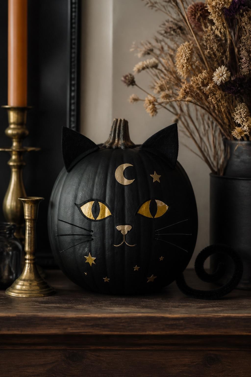 Image Prompt: A realistic DSLR photo of a matte black pumpkin decorated as a sleek black cat, with gold moon and star stickers, pointed felt ears, painted yellow eyes, thin wire whiskers, a curled black pipe cleaner tail, sitting on a dark wood shelf with brass candle holders, dried flowers, and soft moody autumn light, elegant Halloween animal pumpkin design.