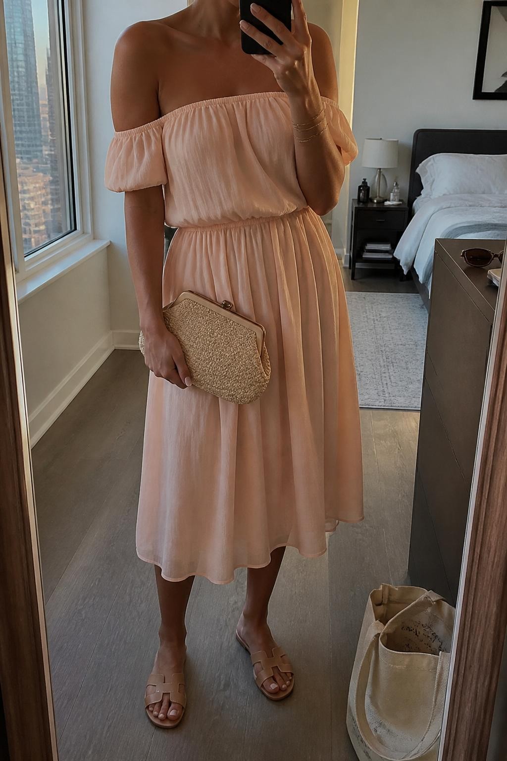 Image prompt
mirror selfie of a woman wearing a soft peach chiffon off-shoulder midi dress, nude flat sandals, small gold hoop earrings, and a raffia clutch with a clean shape, holding a phone in front of a mirror, cropped at NECK so face doesn't show, with a natural casual selfie pose, in a city apartment, evening golden hour, including small lived-in details like a tote bag on the floor, sunglasses on a dresser, or soft bedding in the background, latest iPhone photo quality.